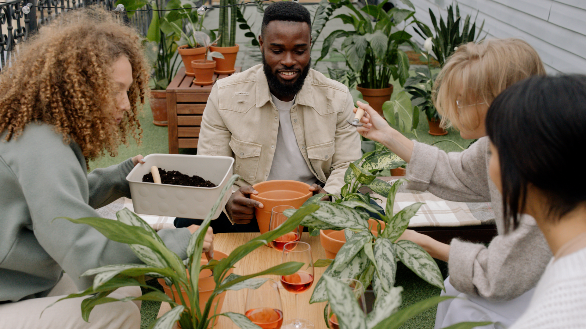 A group of friends sitting around a table, potting plants together in a vibrant outdoor setting.