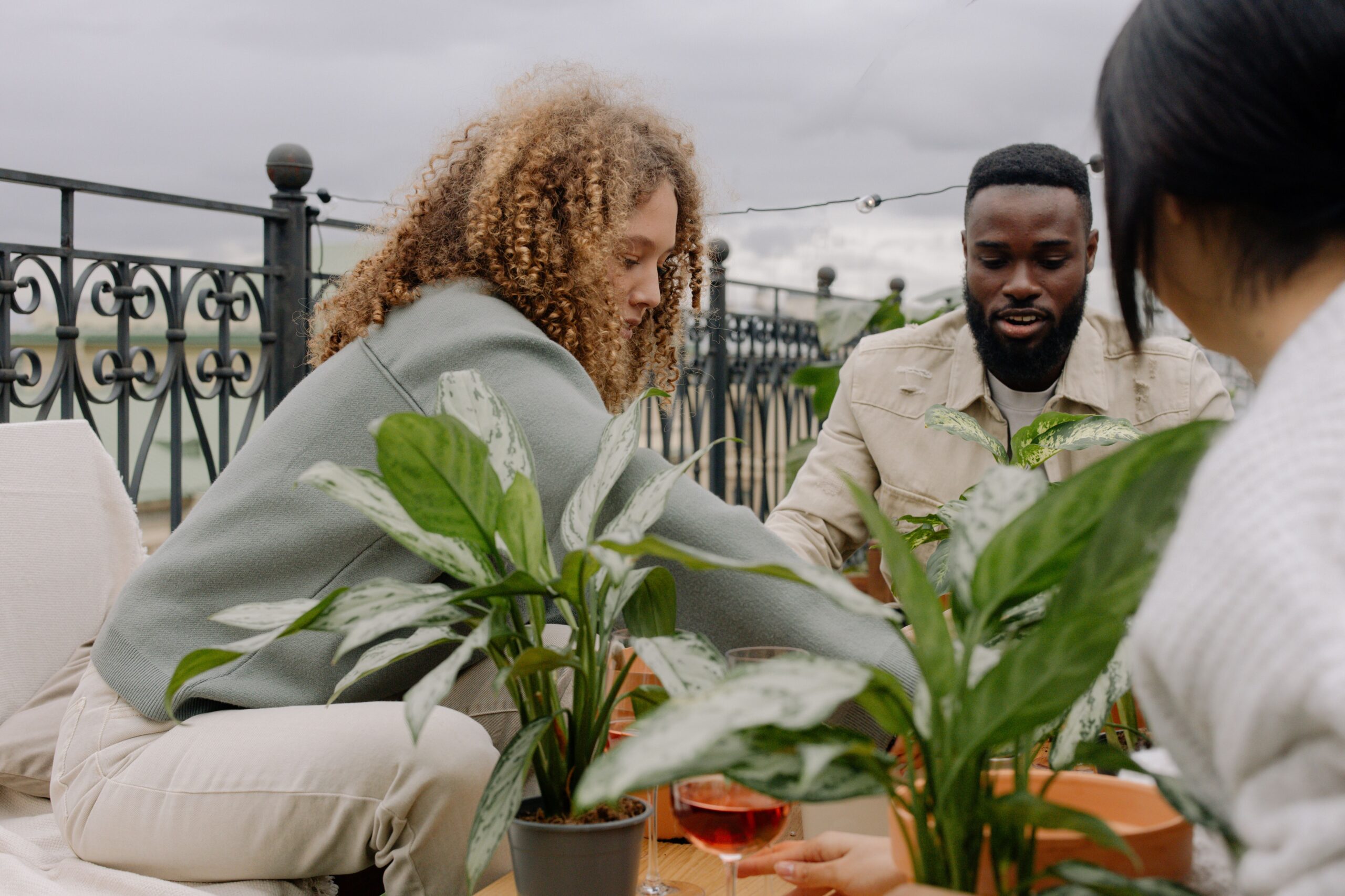 A diverse group of friends gathered outdoors around a table potting plants together at Greenhouse Plants Café